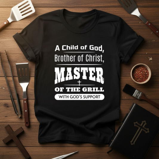 Black t-shirt with text on a wooden surface with grill tools and religious items.