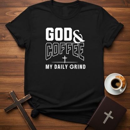 Black t-shirt with 'God & Coffee: My Daily Grind' text on a wooden surface with a cup of coffee and cross.