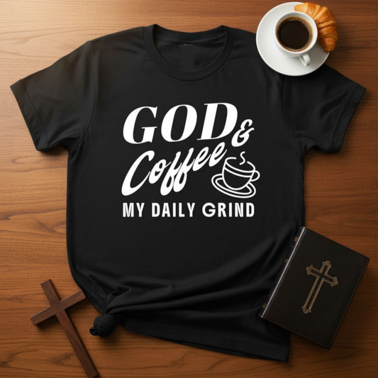 Black t-shirt with 'GOD & Coffee = MY DAILY GRIND' text on a wooden surface with a cup of coffee and croissant.
