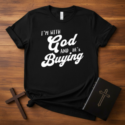 Black t-shirt with 'I'm with God and He's Buying' text on a wooden surface with crosses and a book.