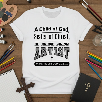 White t-shirt with text 'A Child of God, Sister of Christ, I am an Artist' on a wooden surface with art supplies.