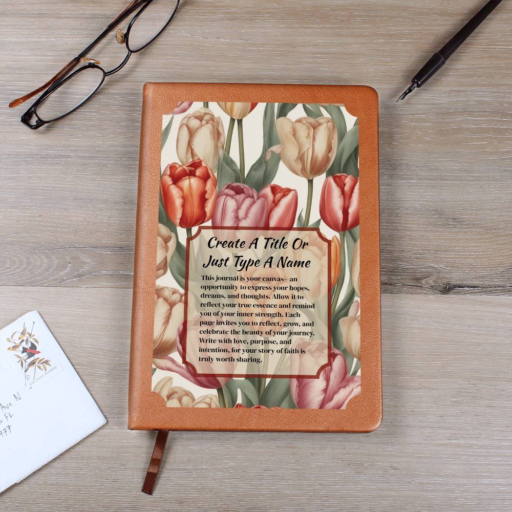 Vegan leather journal with a floral design on the cover, featuring text, red-orange, and pink tulips on a wooden surface with glasses and a pen.