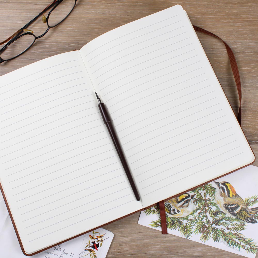 Open notebook with lined pages on a wooden surface, accompanied by a pen and decorative cards.